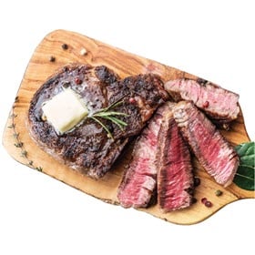 Boneless Ribeye from Dierbergs shown grilled and resting on a wooden board, partially sliced with butter melting on top.