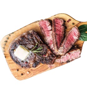 A rib eye steak from Dierbergs shown grilled and resting on a wooden board, partially sliced with butter melting on top.