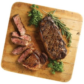 Two NY Strip Steaks from Dierbergs shown grilled and resting on a wooden board, one sliced for serving.