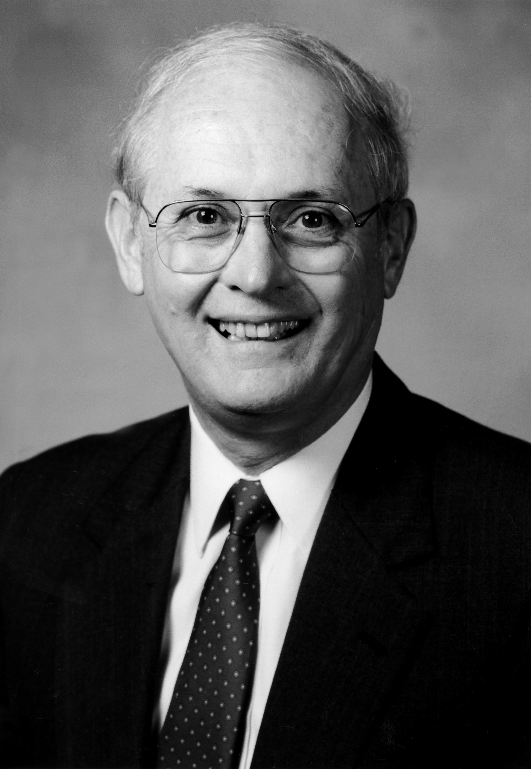 A photo of Roger Dierberg wearing glasses and a suit jacket and tie, smiling for the camera.
